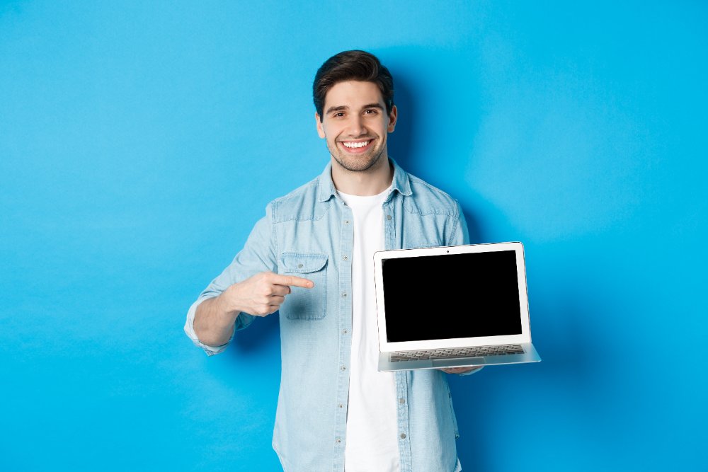 website builder pointing his fingre toward laptop with black screen,