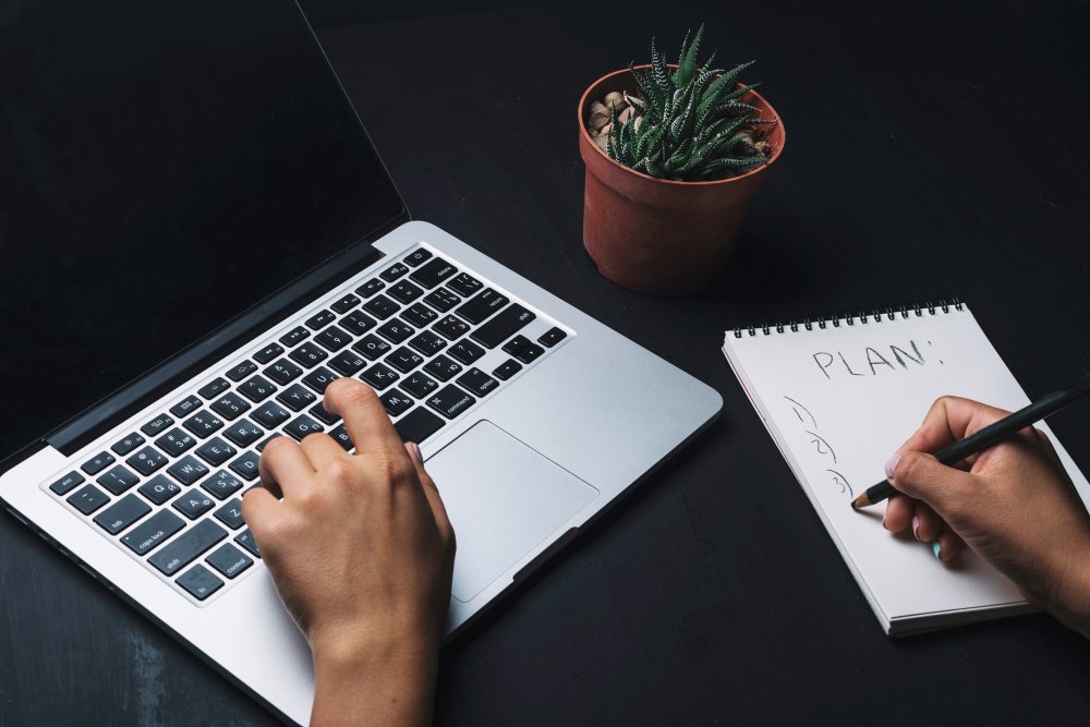 content writer writing with both hand 1 is on laptop and other on paper with pen
